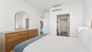 A bedroom with a bed, a dresser, a mirror, and an air conditioning unit. - Two Bedroom Balcony with Private Hot Tub | Near City Center (Salt Lake City)