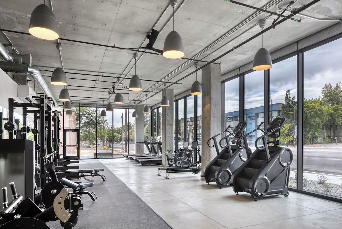 A gym with exercise equipment, large windows, and pendant lighting.