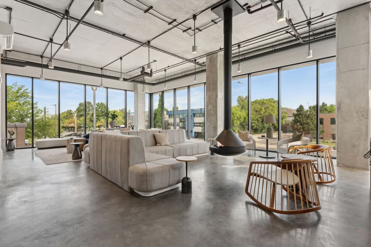 A spacious, modern lounge area with large windows, a high ceiling with exposed pipes, and contemporary furniture.