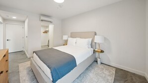 A modern bedroom with a bed, bedside tables, and a door leading to a bathroom. - Modern One bedroom Unit w/ Private Laundry access in Placemakr Salt Lake City (Salt Lake City)