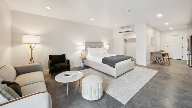 A modern hotel room with a bed, a sofa, a chair, a small table, and an air conditioning unit. - 1 Studio Unit Near Downtown SLC | Modern stay in Salt Lake City Downtown (Salt Lake City)