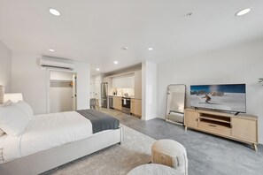 Una habitación de hotel moderna con cama, televisor, kitchenette y aire acondicionado.