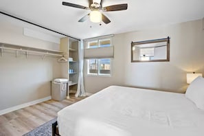 Ein Schlafzimmer mit Bett, Deckenventilator, Fenster, Spiegel und begehbarem Kleiderschrank.