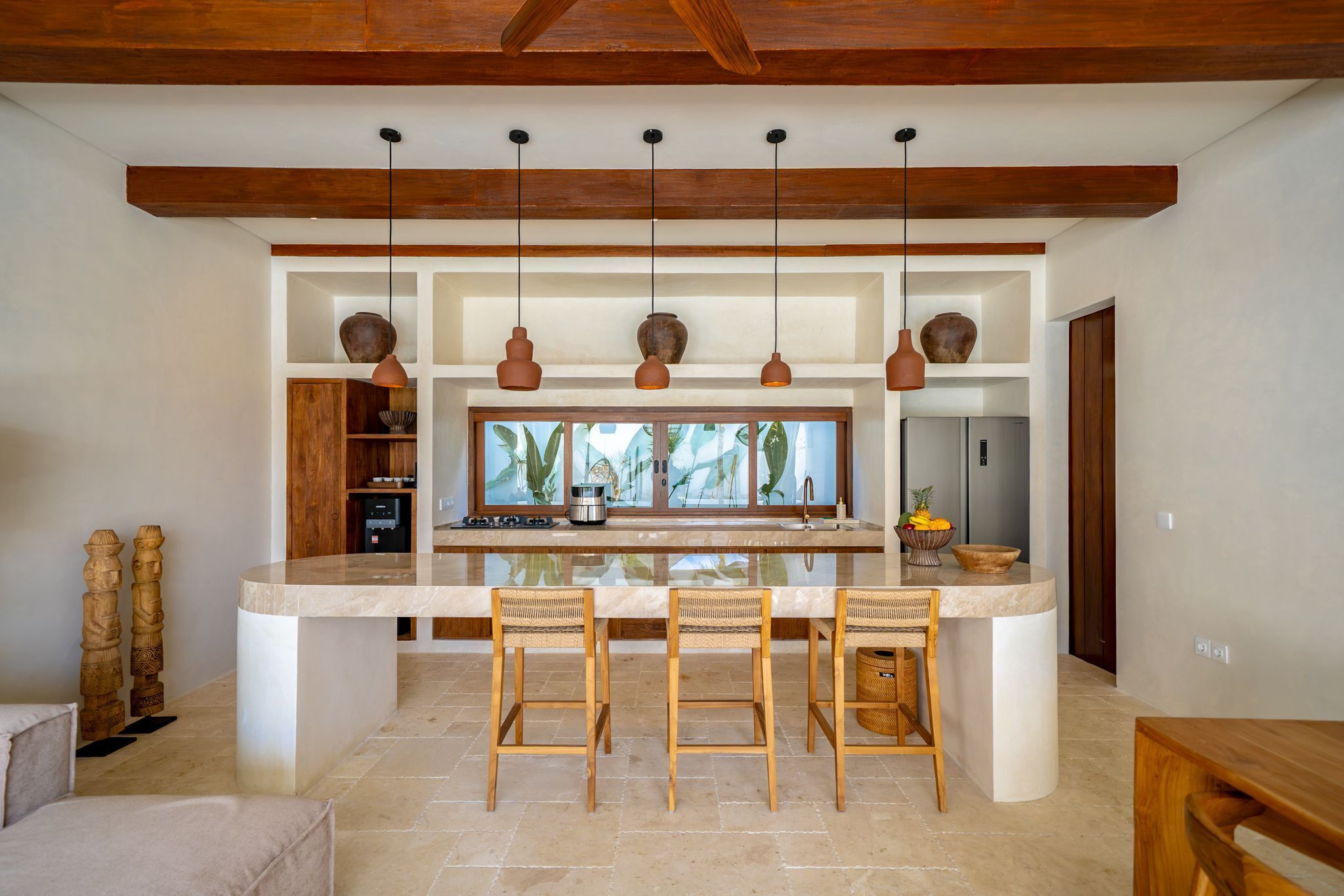 Una cocina moderna con una isla central, luces colgantes y vistas por la ventana.