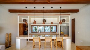 Una cocina moderna con una isla central, luces colgantes y vistas por la ventana.