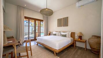 A hotel room with a bed, a desk, a chair, a lamp, a bedside table, and a large vase.