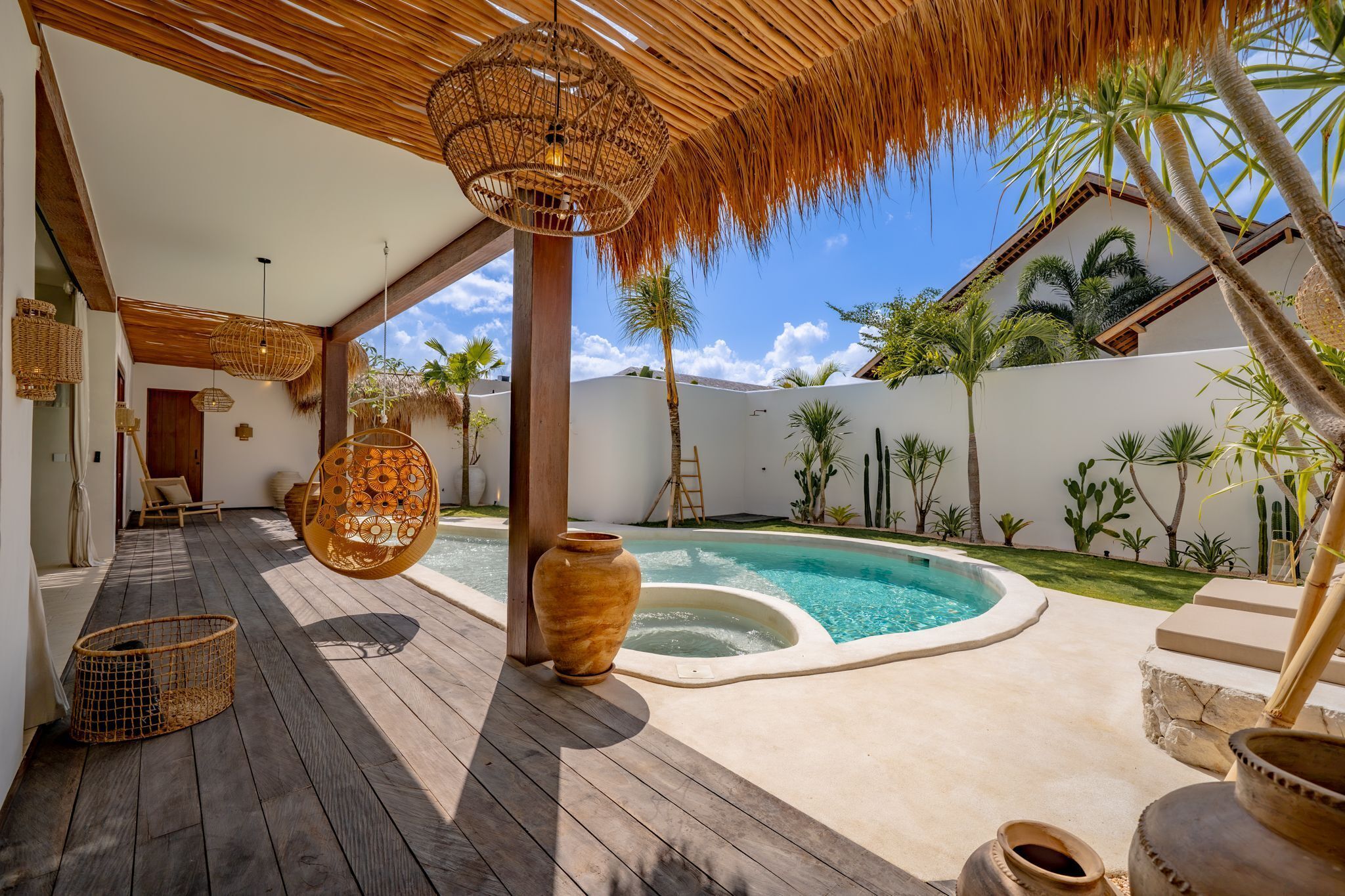 A wooden deck with a pool, wicker furniture, and tropical plants.