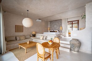 Una sala moderna con sofá, mesa de centro, mesa de comedor y sillas. Hay un jarrón grande y un frutero sobre la mesa.