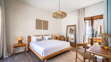 A hotel room with a wooden bed, two bedside tables, a desk with a chair, a large mirror, and a hanging light fixture.