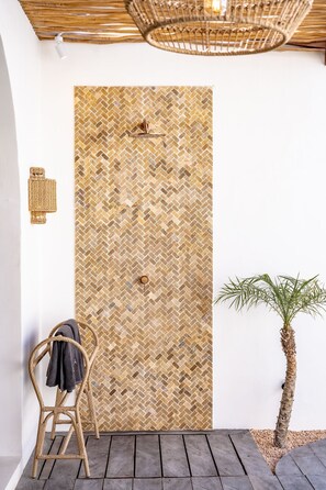 A room with a herringbone-patterned wall, a wicker chair, a small palm tree, and a wooden floor. - Amaka Villas Uluwatu (Uluwatu)