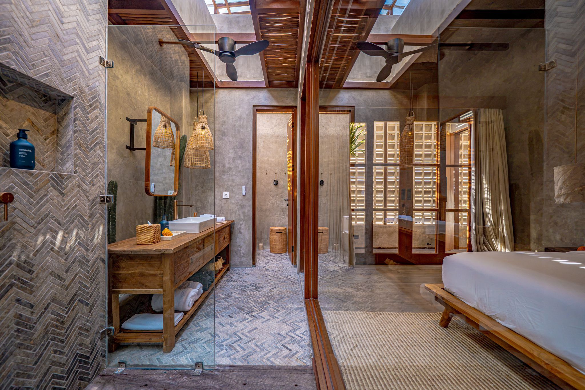 A modern bathroom with a herringbone tile floor, a wooden vanity, a large mirror, and a shower area.