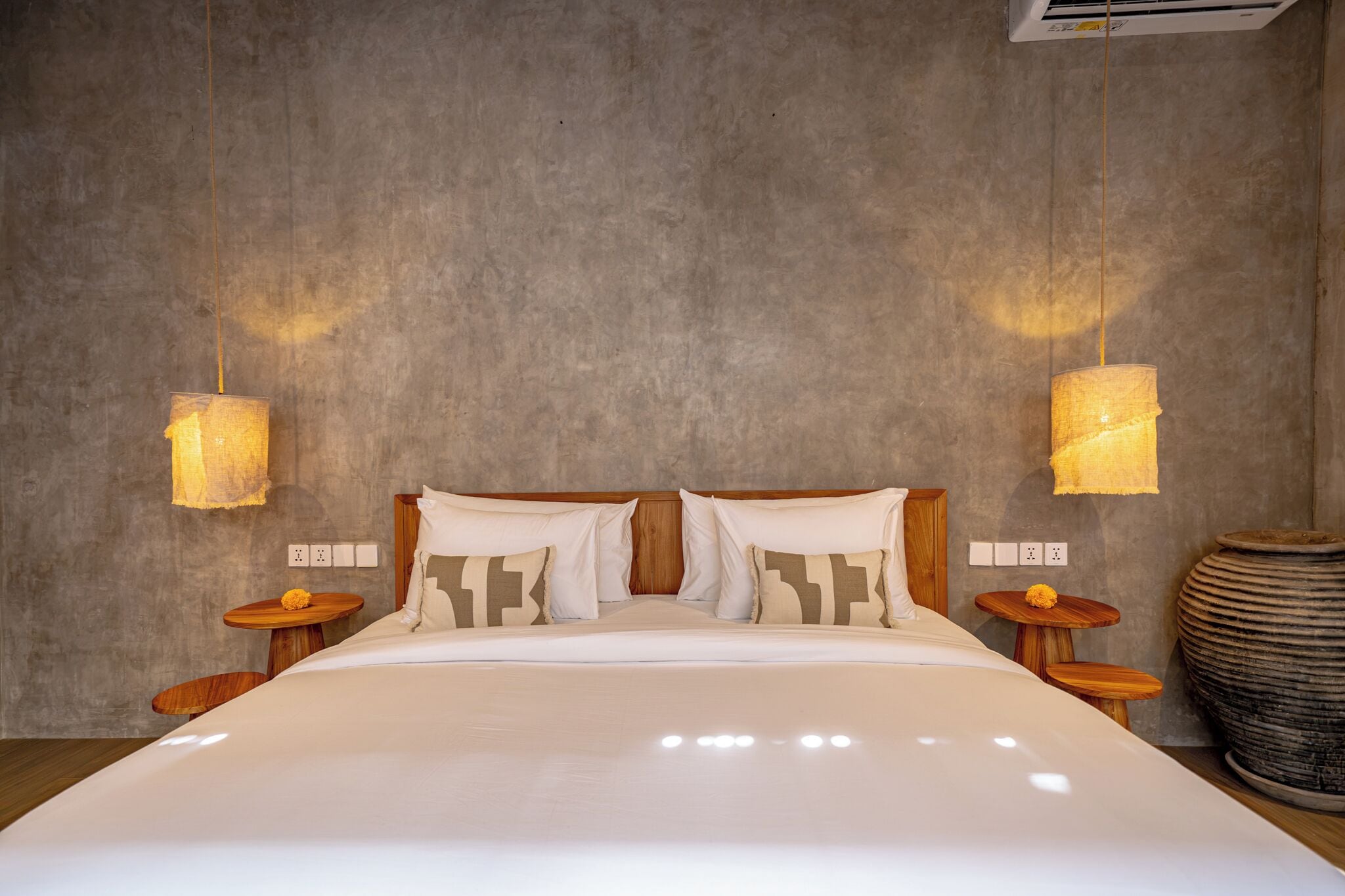 A bedroom with a large bed, two bedside tables, a wall-mounted air conditioner, and a textured wall.