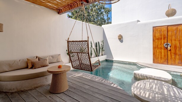 Un área junto a la piscina con una silla colgante, un sofá y una puerta de madera.