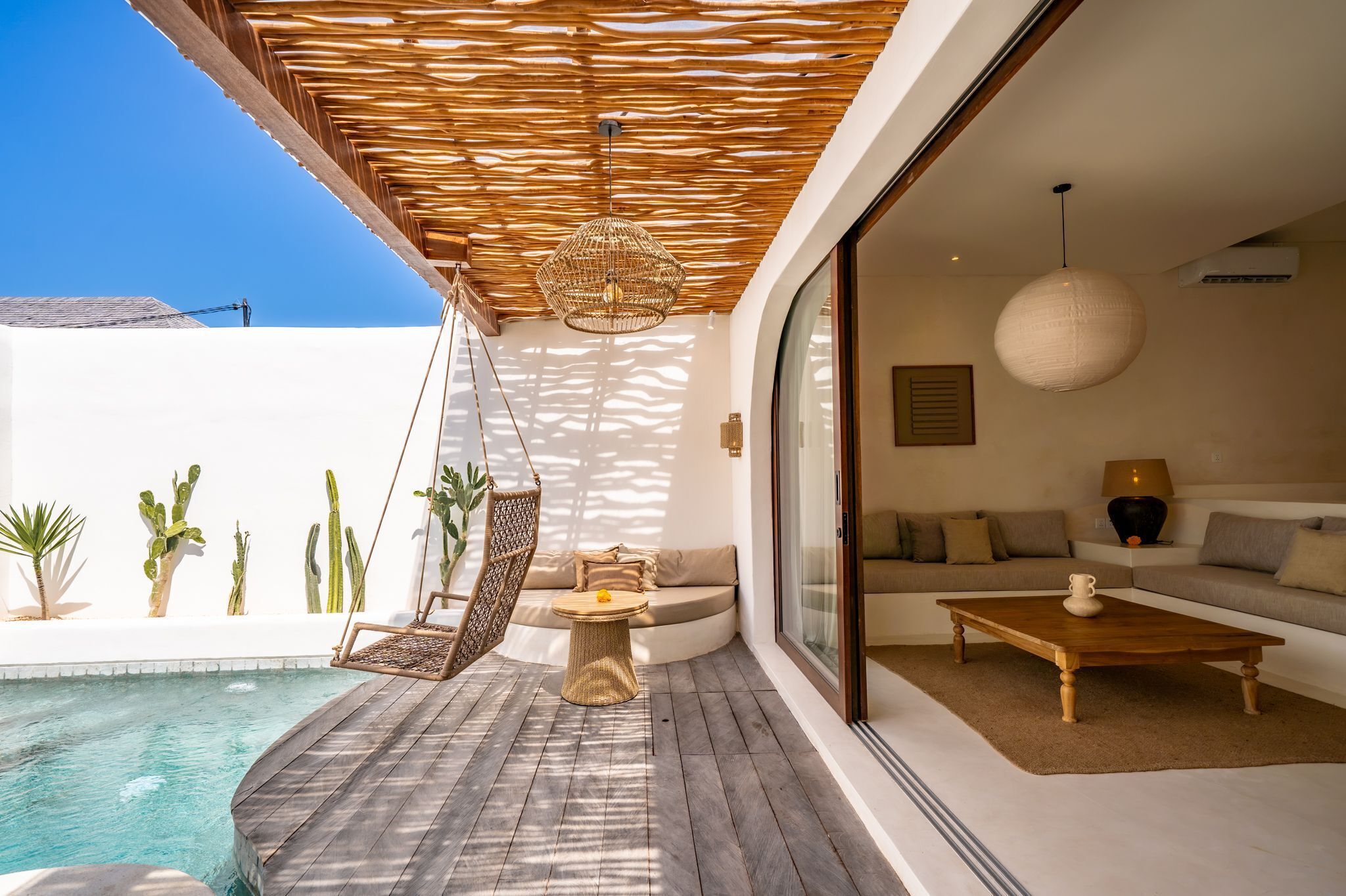 A modern outdoor living area with a pool, a hanging chair, a sofa, and a coffee table.