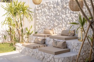 Pared de pedra com área de estar integrada, almofadas e um candeeiro de vidro.