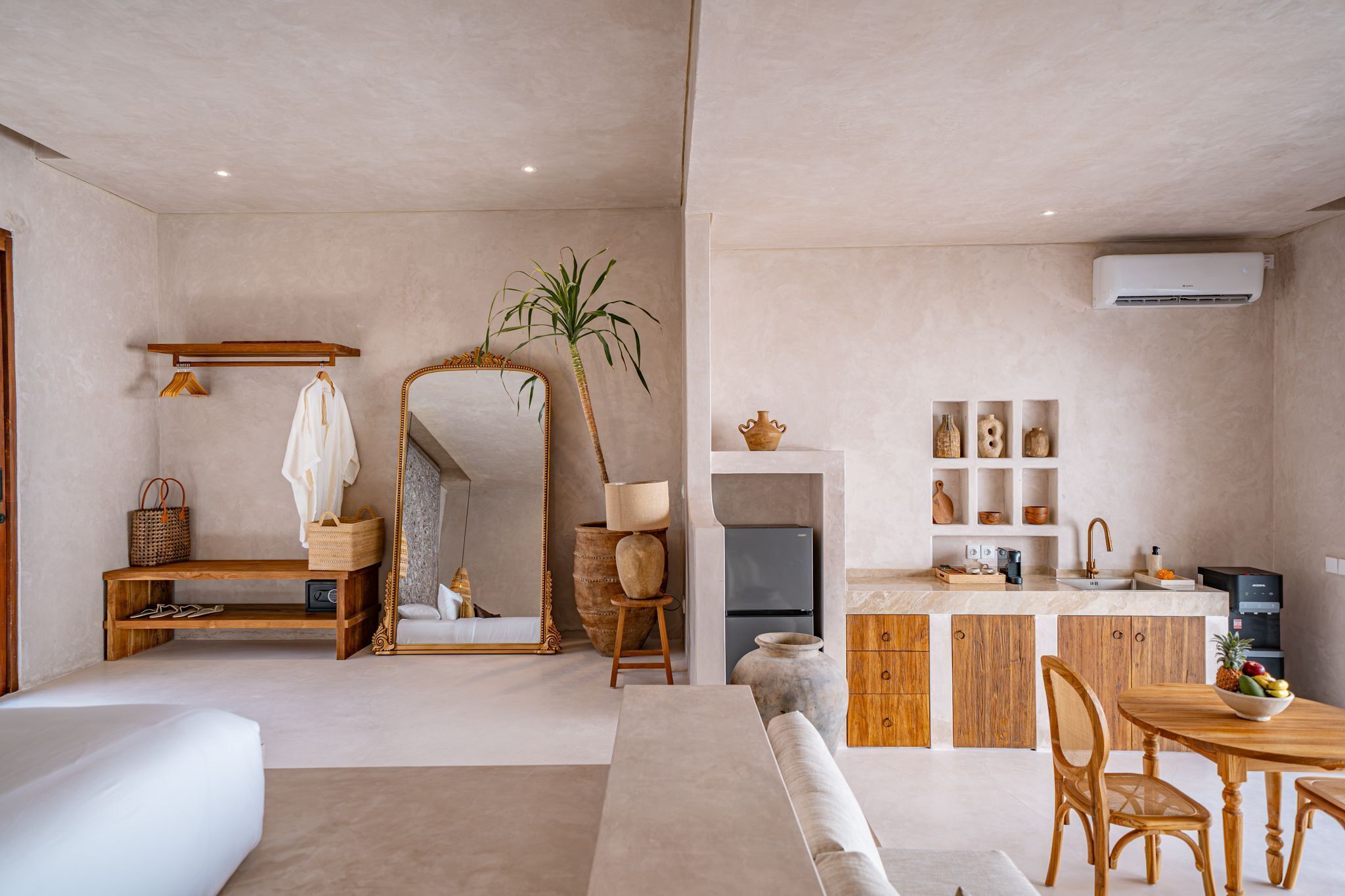 A modern living room with a sofa, a dining table with chairs, a kitchen area with a refrigerator, and a large mirror.