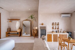 A modern living room with a sofa, a dining table with chairs, a kitchen area with a refrigerator, and a large mirror. - Amaka Villas Uluwatu (Uluwatu)