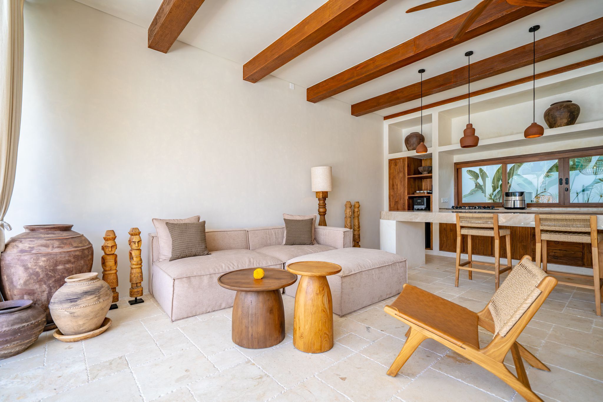 A modern living room with a sofa, two wooden side tables, a wooden bench, and a kitchen area with a dining table and chairs.