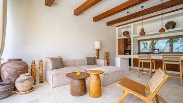 A modern living room with a sofa, two wooden side tables, a wooden bench, and a kitchen area with a dining table and chairs.