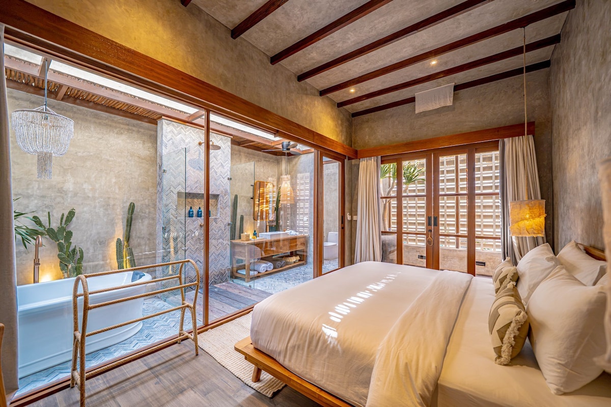Un dormitorio amplio con una cama grande, ducha envuelta en vidrio y vista a un patio.