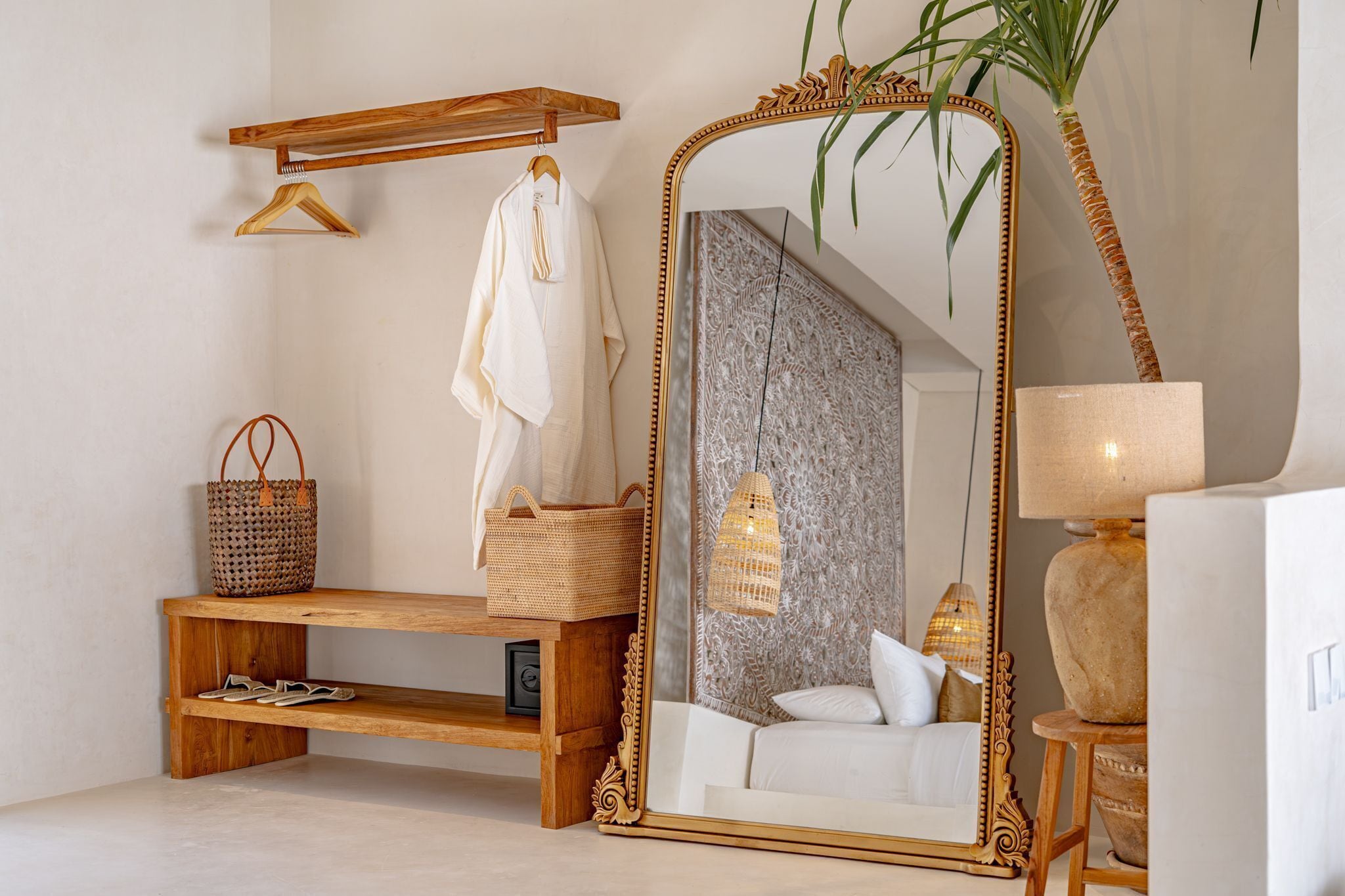 A bathroom with a large ornate mirror, a wooden bench, a hanging towel, a woven basket, and a plant.