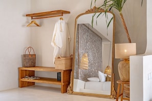 Un baño con un espejo grande y ornamentado, un banco de madera, una toalla colgada, una cesta tejida y una planta.