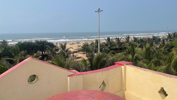 A coastal view with a beach, palm trees, and a clear sky. - Sita Niwas Holiday Home Resort (Puri)