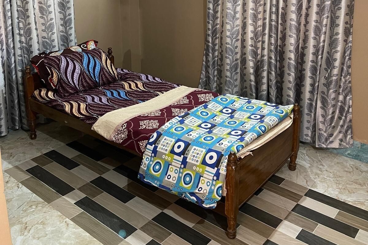 Uma cama de solteiro com roupa de cama estampada, cortinas com desenho de folhas e um chão de azulejos com padrão quadriculado.