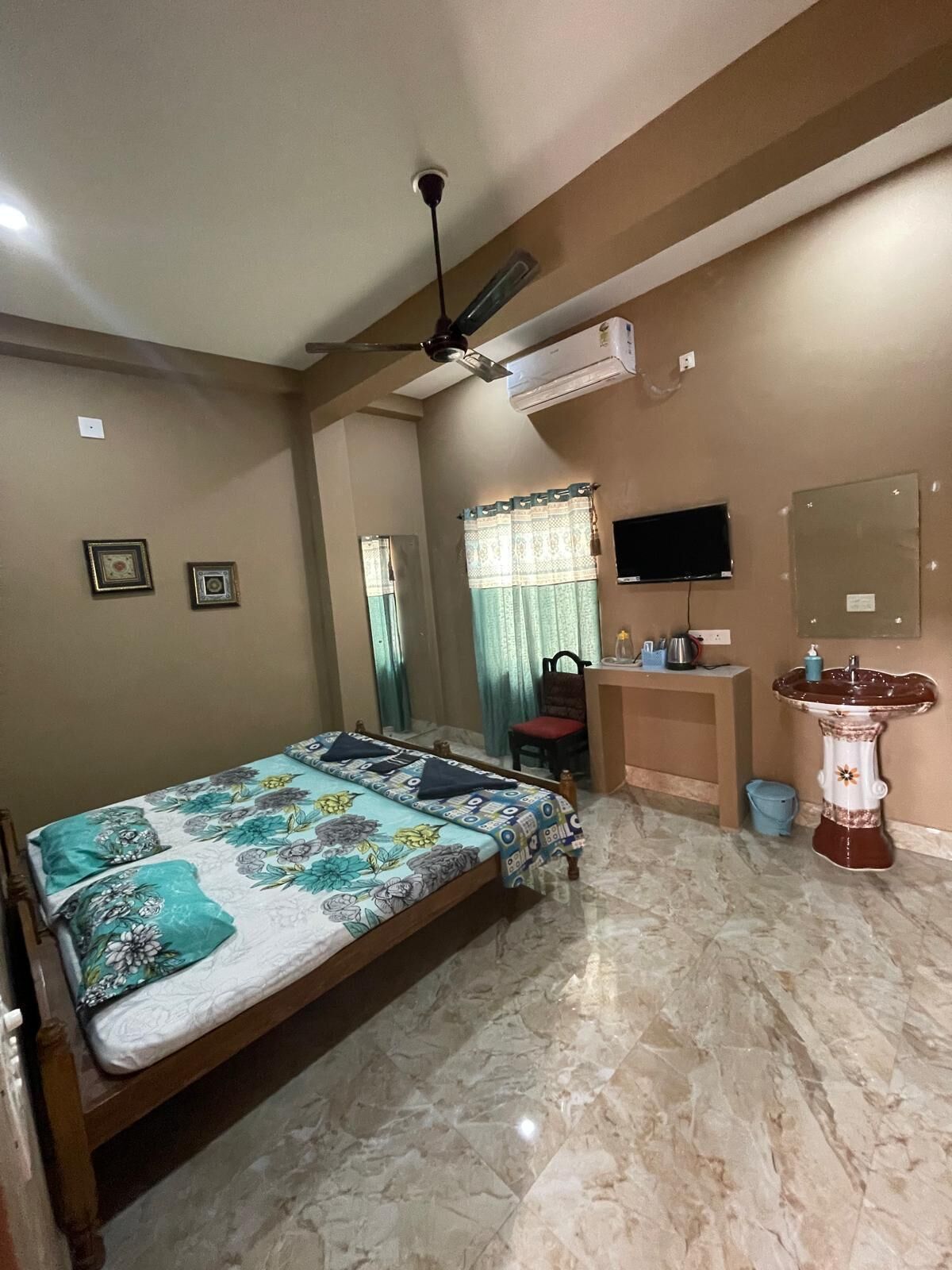 A bedroom with a bed, a desk, a chair, a television, and a bathroom with a sink and mirror.