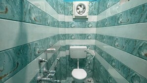 A bathroom with a toilet, a hand dryer, and a fan. - Sita Niwas Holiday Home Resort (Puri)