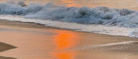A beach with waves and a sunset.