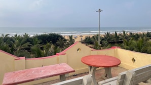 A beach view from a balcony with a table and bench, overlooking the ocean and palm trees. - Sita Niwas Holiday Home Resort (Puri)
