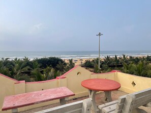 Vista da praia a partir de uma varanda com mesa e banco, com vista para o oceano e palmeiras.
