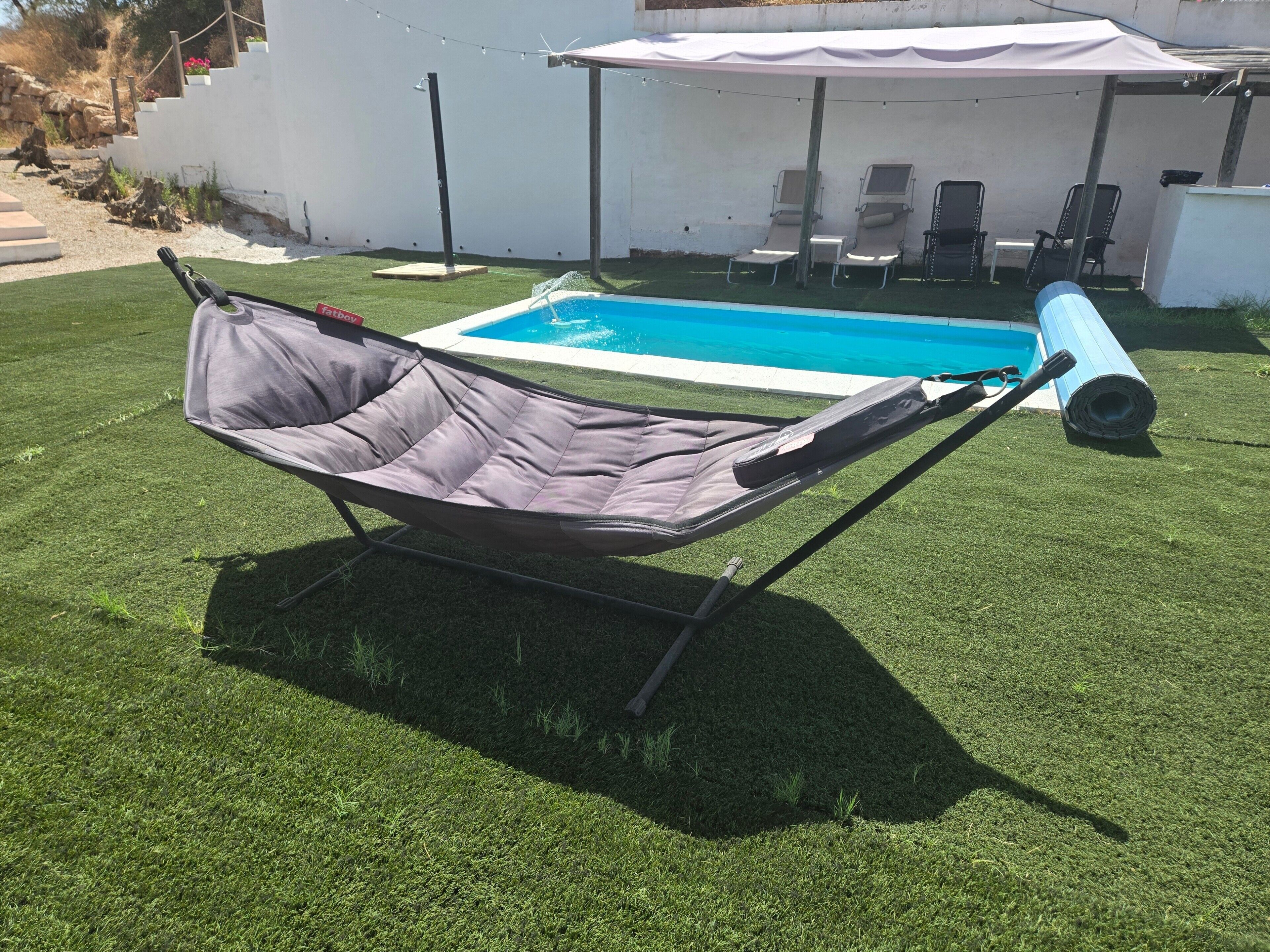 A hammock chair on artificial grass with a pool in the background.