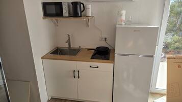 Una cucina compatta con microonde, bollitore e frigorifero.