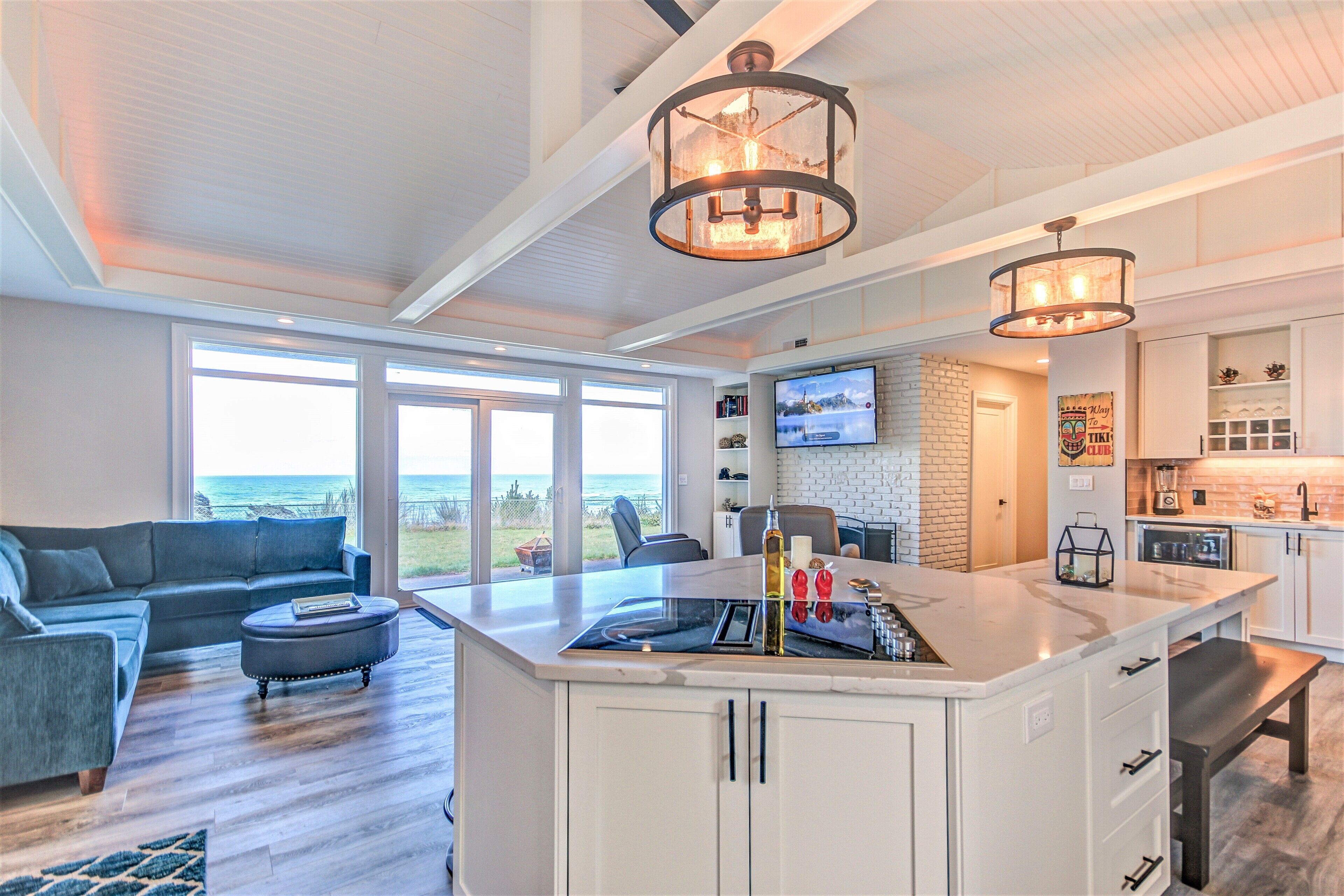 A modern kitchen with a central island, a dining area with a sofa, and a large window offering a view of the ocean.