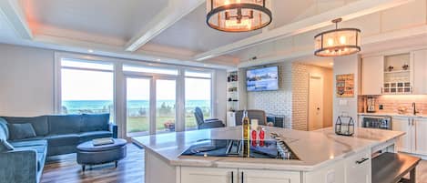 A modern kitchen with a central island, a dining area with a sofa, and a large window offering a view of the ocean.