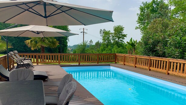 Ein Schwimmbecken mit Holzterrasse, Liegestühlen und Sonnenschirmen.
