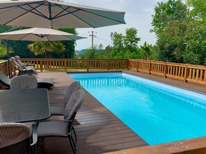 Une piscine entourée d’une terrasse en bois, de chaises longues et de parasols.