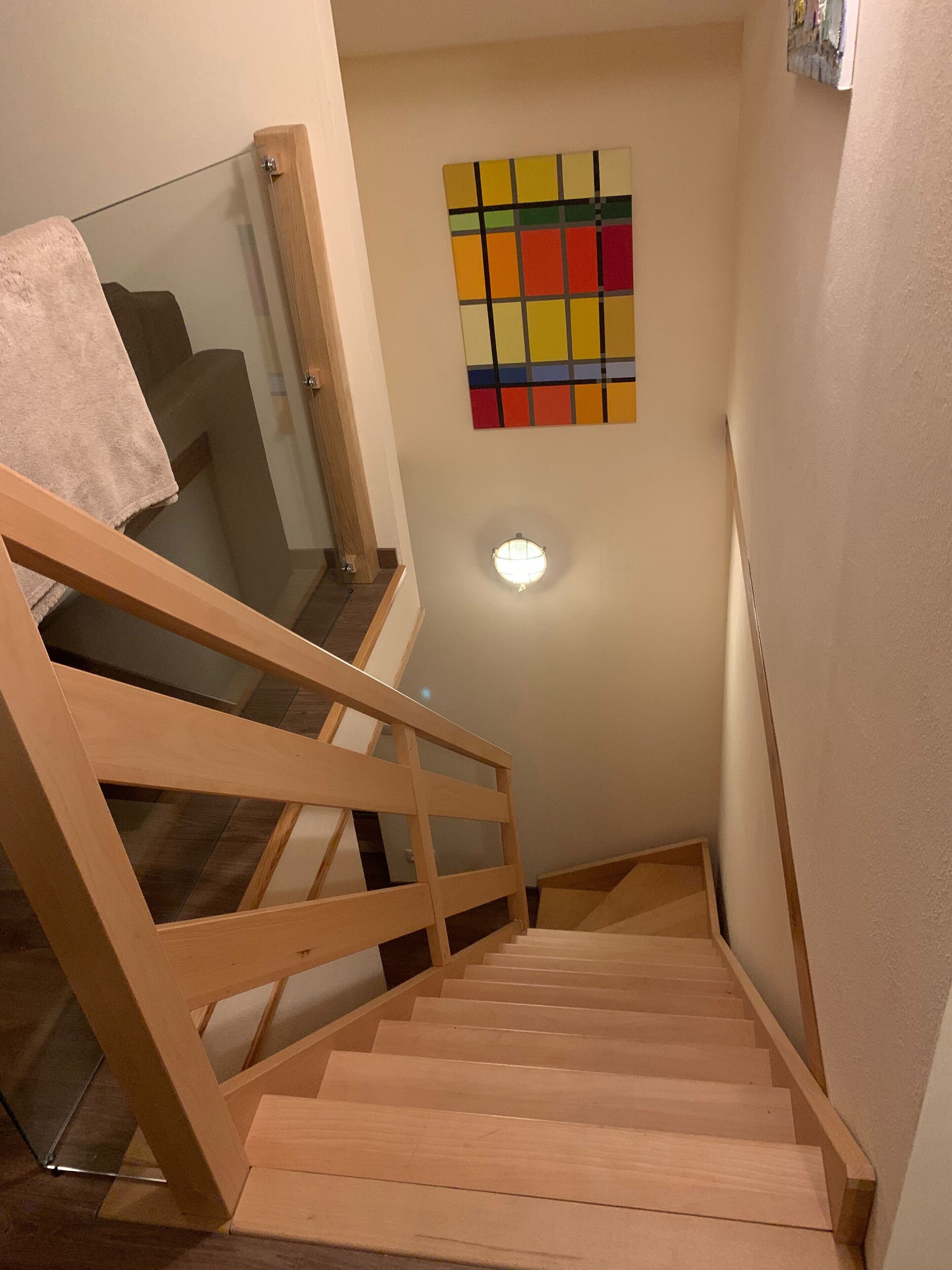 Eine Holztreppe mit Glastrennwand führt zu einer Zwischenebene.