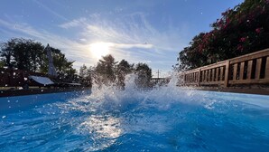 Ein Schwimmbecken mit spritzendem Wasser, umgeben von einer Holzterrasse und Bäumen.