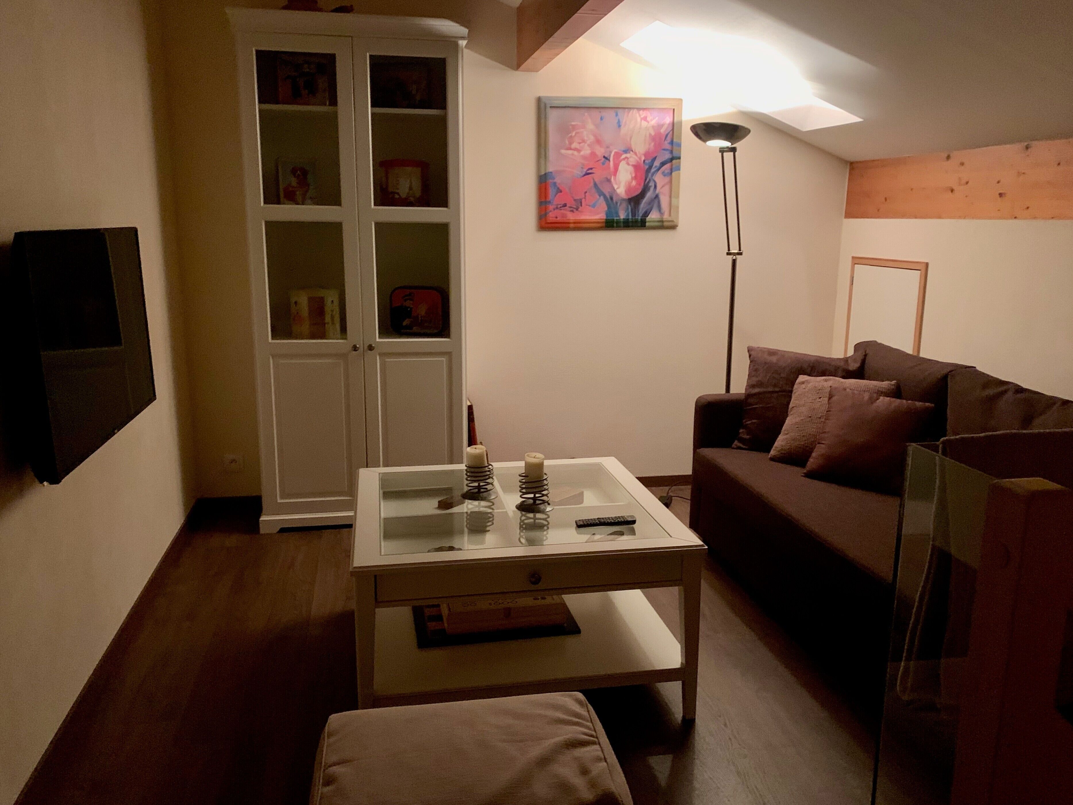 Ein Wohnzimmer mit einem Glastisch, einem braunen Sofa, einer weißen Kommode und einem Bild an der Wand.