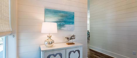 A hallway with a white wall, a painting of a blue sky and sea, a lamp, and a decorative cabinet.