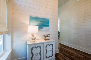Un corridoio con una parete bianca, un quadro raffigurante cielo e mare azzurri, una lampada e un mobile decorativo.
