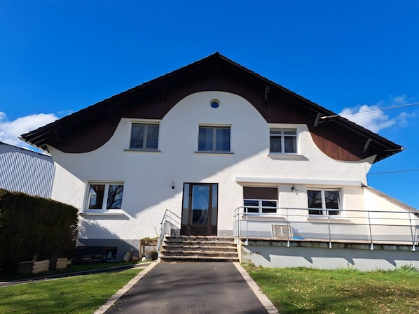 A two-story house with a front entrance, a staircase, and a clear sky. - “Au Bonheur De La Chaux” Apartment with Private Terrace, Garden, and Wi-Fi (Damprichard)