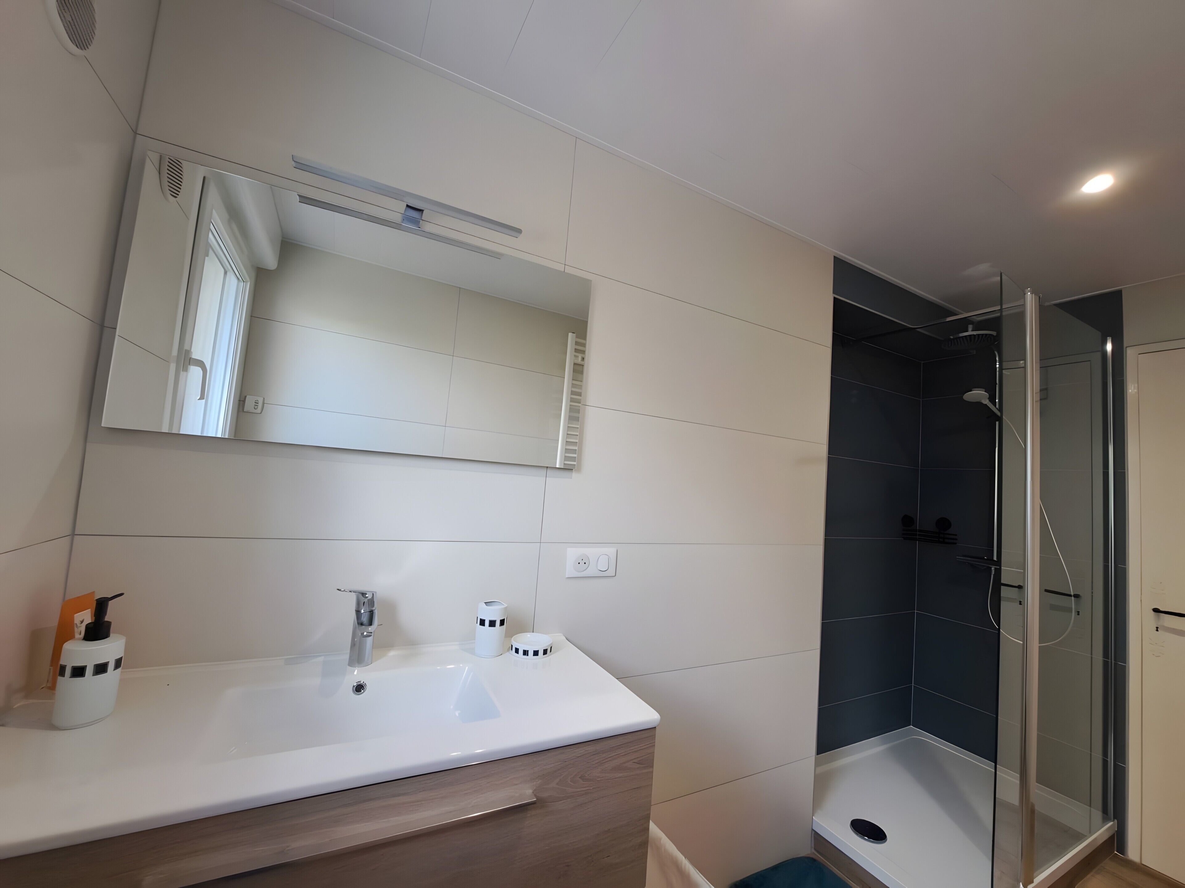 Een badkamer met een witte wastafel, een spiegel, een douche met een glazen deur en een betegelde vloer.