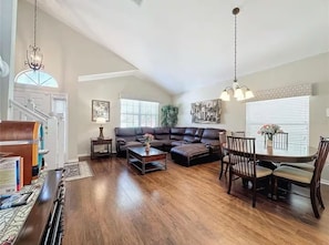 A spacious living room with a sectional sofa, a dining table with chairs, and a chandelier. - Our Happy Place! FREE Pool Heat (Davenport)
