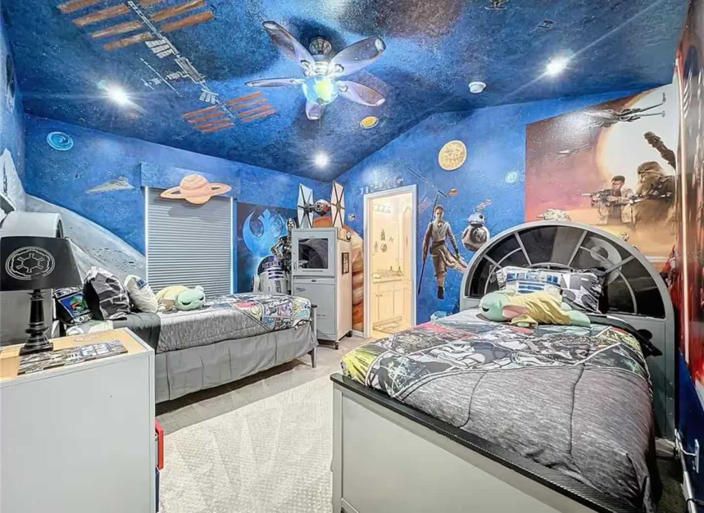 Een slaapkamer met twee bedden, een plafondventilator en muurdecoratie met een ruimte thema.