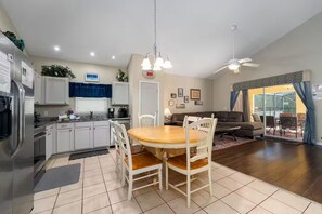 A modern kitchen with white cabinets, a dining table with chairs, a ceiling fan, and a sliding glass door leading to an outdoor area. - Our Happy Place! FREE Pool Heat (Davenport)