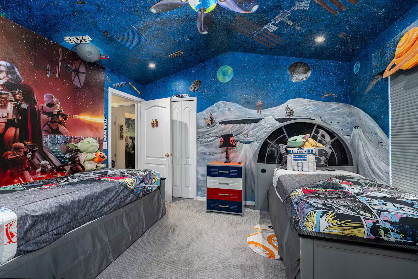 Una habitació amb un mural temàtic espacial, dos llits, un taulell i una porta.